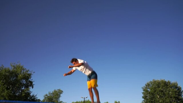 Young sports acrobat jumping on a trampoline. back flip. european guy in beachwear on blue sky background