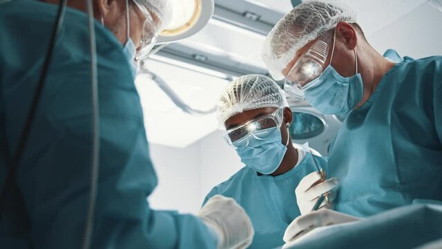 Multi-race corporate medical coworking team with chief surgeon performing surgical procedure in emergency department. Operation room. Healthcare.