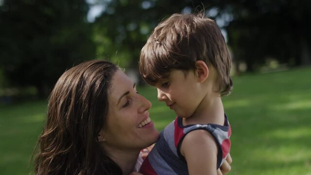 Close-up of a beautiful mother talking to and kissing her young son at the park