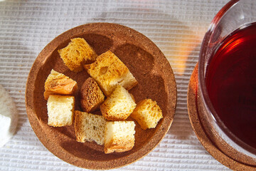 Square toasted pieces of homemade delicious rusk, hardtack, Dryasdust, zwieback on a plate and black tee in a cap on a white tablecloth.