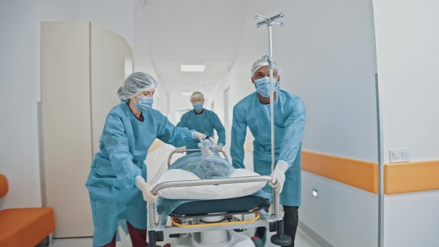 Group of young multi-ethnic paramedic doctors hurrying running through hospital corridor moving seriously injured patient to surgical room for immediate surgery.