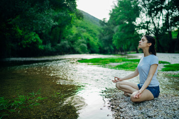 Meditation yoga woman siting at Lotus position on the shore of river.Serenity and yoga practice.Healthy lifestyle.Self isolation in nature.Lockdown beach trip.Mindfulness.Breathing exercise