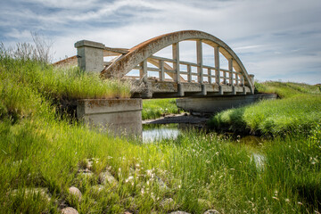 Fototapeta na wymiar The old lichen-covered concrete bridge in Cadillac, SK with green grass in foreground