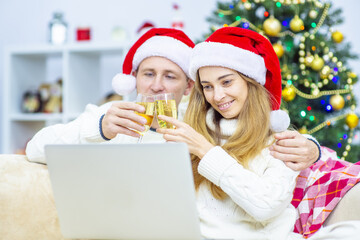 Young couple at home in santa hats congratulating relatives on christmas or happy new year bumping champagne online