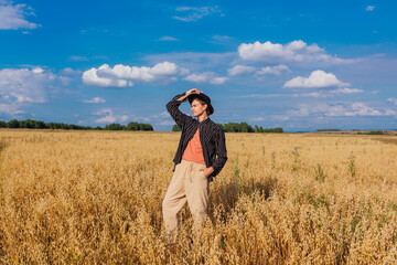 Naklejka na ściany i meble Tall handsome man with black hat standing at golden oat field.