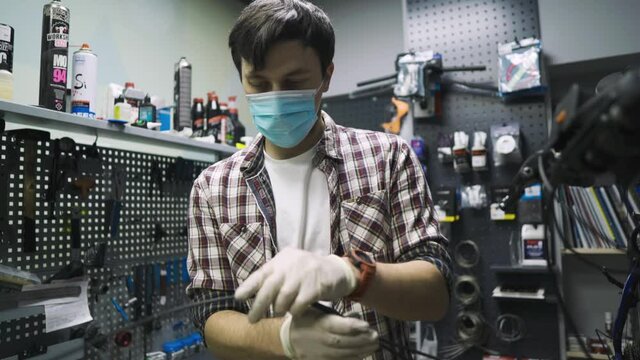 Service engineer performs diagnostics and repairs on bicycle in professional workshop, wearing protective mask and safety gloves from client covid 19. Service topic during coronavirus pandemic
