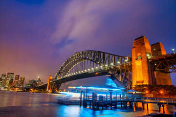 Naklejka premium Sydney Harbour Bridge at night with ferry boat crossing and city skyline