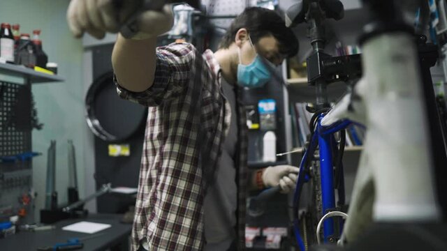 Theme service maintenance and repair of bike in bicycle store during coronavirus epidemic. Mechanic repairs mountain cycle wearing protective mask, new rules covid 19. Subject workman profession