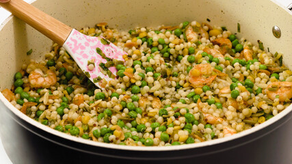 A savory blend of pearled couscous, orzo, baby garbanzo beans, red quinoa, shrimp, green peas close up on frying pan