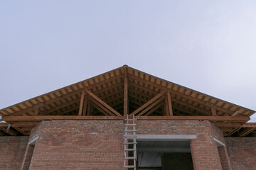 Fototapeta na wymiar Roof on a brick house. Wooden logs, rafters, racks. Roof construction concept for low-rise construction.