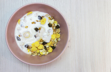 muesli with on a pink plate, top view. Muesli with fresh milk, yogurt or kefir. Muesli is made from oatmeal, a mixture of multi-grain flakes with dried fruits, nuts and sunflower seeds. on a white