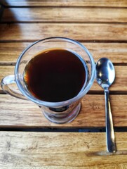 espresso coffee in a transparent glass cup with a tea spoon on a wooden table high angle shot