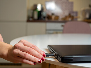 Fototapeta premium female manicured hand plugging usb, connecting USB flash drive in white laptop, kitchen in a flat. Plugging removable flash disk. Woman hand is using the USB while working at home during Covid-19