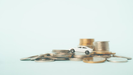 white miniature car on pile of coins with blue-green background , business and finance background