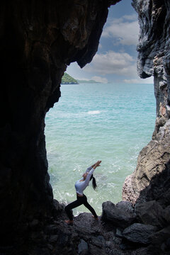 Caucasian woman practicing yoga in a cave near the sea