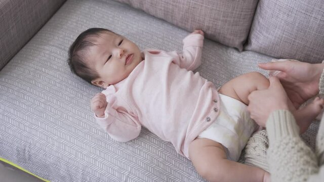 innocent newborn baby on the couch at home is looking at its mommy while she is doing up the bodysuit buttons after done changing the diaper.