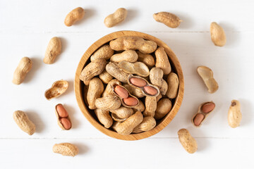 Top view of peanuts in a wooden bowl on white background,
