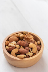 Portrait view of mixed nuts in a wooden bowl on white background