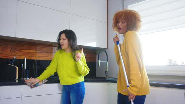 Best Friends Roommates Having Fun While Cleaning Kitchen. Singing And Dancing With Mop. High Quality Photo