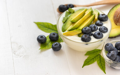 Organic yogurt topped with avocado and blueberry on white wooden background, healthy and nutritious diet