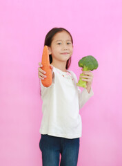 Little asian girl showing carrot standing isolated on pink background. Kid and vegetable concept. Focus at carrot in hand