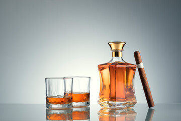 close up view of cigar, bottle of whiskey  and a glasses aside on grey back. 