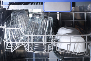 A man loads dirty dishes, plates, spoons, forks, cutlery into dishwasher tray.