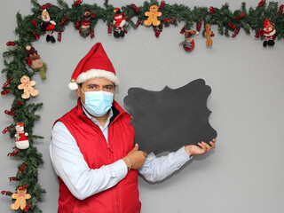 latin man with protection mask and blackboard to write message, in christmas decoration, new normal...