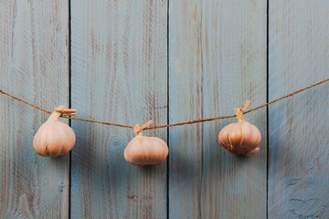 Three whole heads of garlic hanging on the rope on a blue rustic wooden background - Powered by Adobe