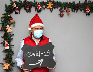 Latino man with protection mask, Santa Claus hat and blackboard with 