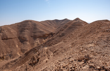 Hikers on a hiking trail in a remote desert region. Panoramic desert landscape of colorful sandy hills, dry wadies, rock formations and boulders.