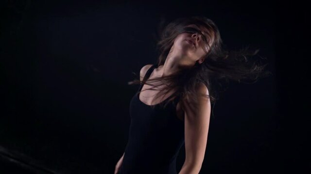 Beautiful, energetic, plastic woman in a black suit in the Studio on a dark background moves and dances.