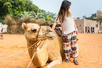 A Camel for the tourist riding and a woman standing in the Heritage folk village in Abu Dhabi, United Arab Emirates.