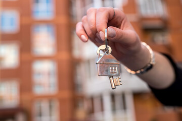 female hand holding keys in front of a new home