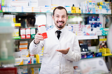 Fototapeta na wymiar Positive male pharmacist showing right drug in pharmacy