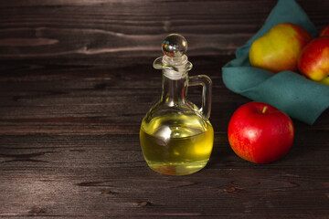Apple cider vinegar in a glass decanter on a dark wooden table. Apples nearby. Free space.