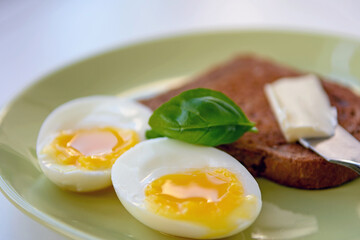 Two soft-boiled egg halves on a plate. Basil leaf, toast and butter. Close up.