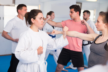 Fototapeta na wymiar Females with males are practicing new karate moves in pairs in class.