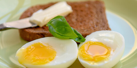 Two soft-boiled egg halves on a plate. Basil leaf, toast and butter. Close up.