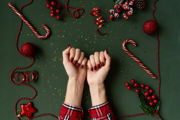 Christmas manicure. Red nails, hands in checkered shirt on green background with red christmas baubles as frame.