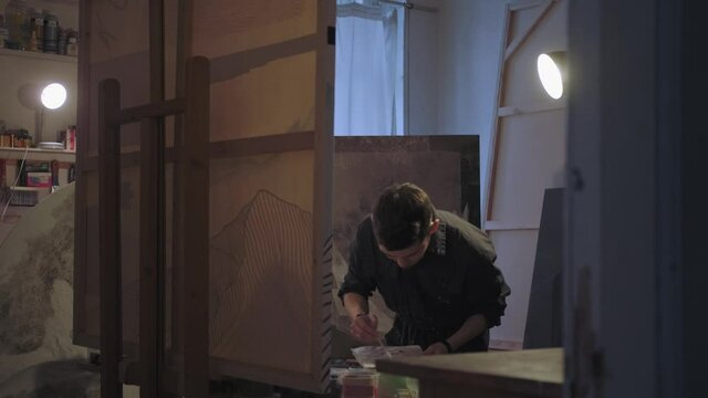 A male artist works in creative workshop on a painting on canvas