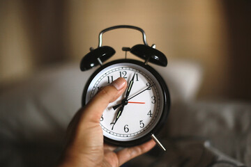 Man hand holding classic black alarm clock showing seven o'clock with blurry background, waking up in the morning concept
