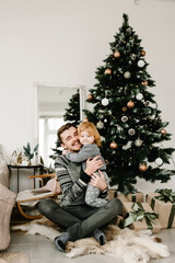 Obraz na płótnie Canvas Father and little child having fun and playing together at home. Portrait loving family close up. Cheerful dad hugging cute baby daughter girl near Christmas tree. Merry Christmas and Happy Holidays.