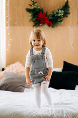 Happy little girl inwaiting for Merry Christmas playing on a bed decorated