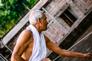 Close-up Portrait of Indian Senior Man Arching. Happy alone side facing old man, wearing white dress, giving pose with style at the camera. Elderly Man Is Enjoying Retirement In Nature In Afternoon.