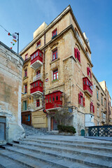 Fototapeta na wymiar View on street of the ancient city of Valletta in evening colors. Red windows and balconies on stone palace. No people. Holidays in Malta.