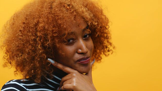 Young african american black woman with curly afro hair and long nails posing in front of yellow background. High quality photo