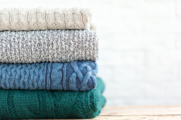 Stack folded of cozy knitted sweaters on white and wooden background.