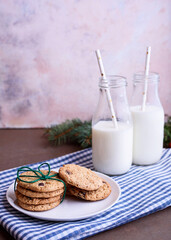 Fresh delicious milk in a glass bottle on a textured background with chocolate cookies on a white plate.