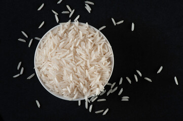 Basmati rice in white bowl on black background. Flat lay.